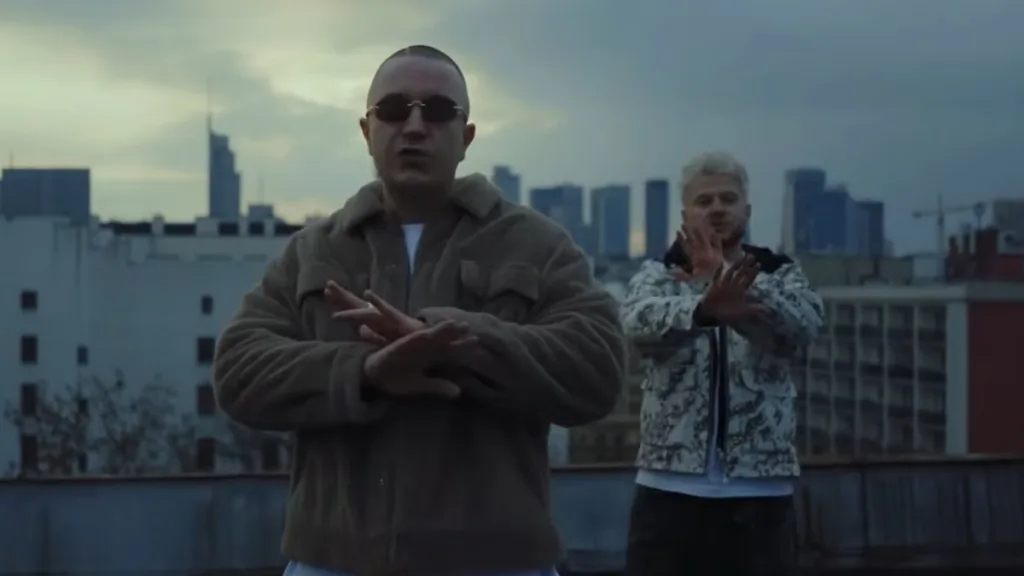 Kadr z teledysku "Nadzieja": raperzy Zbuku (w brązowej, futrzanej kurtce i okularach przeciwsłonecznych) oraz B.R.O (z jasnymi włosami, w białej kurtce we wzory) stoją na dachu budynku w Warszawie.